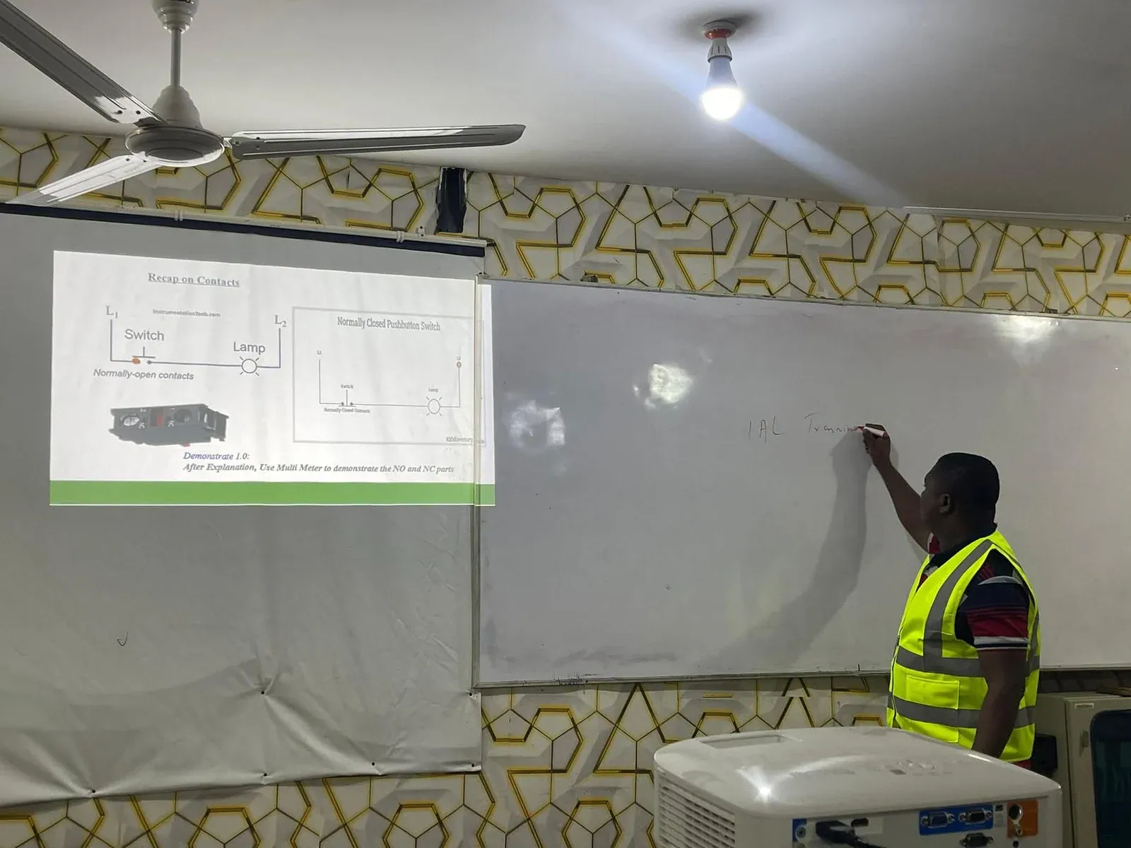 Instructor in a hi-vis vest teaching a circuit diagram lesson beside a projector screen