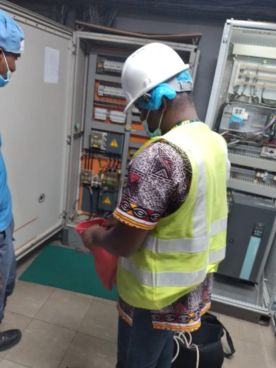 Engineer in a hard hat recording measurements at an industrial control panel